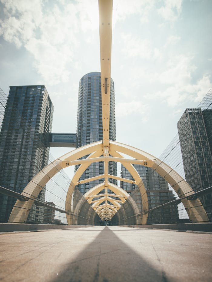 Modern urban arch bridge with towering skyscrapers in the backdrop at dusk, showcasing contemporary architecture.